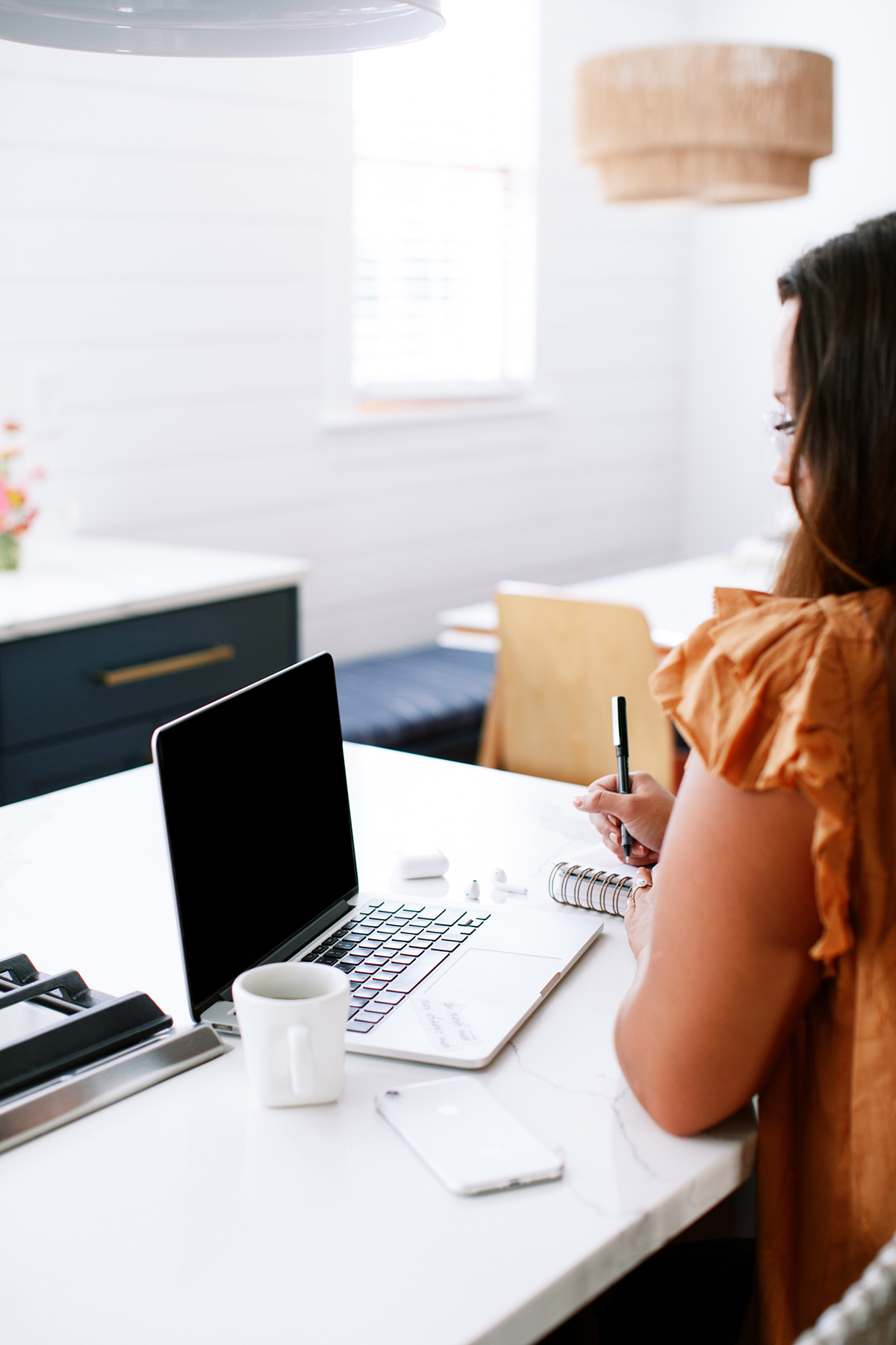 Midlife woman focused on laptop and notebook, representing the value of hard work in business.